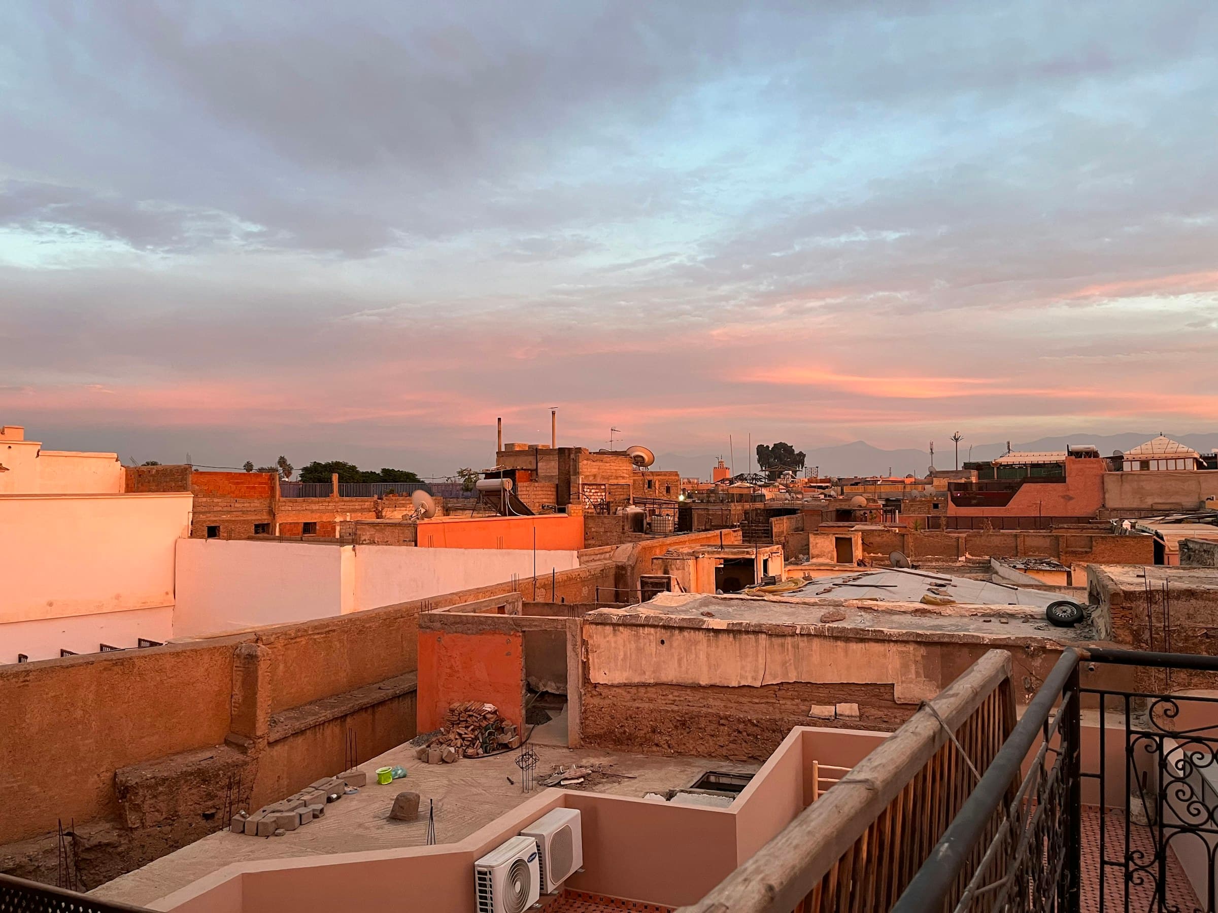 Marrakech medina rooftops glowing pink at sunset, the High Atlas on the far horizon